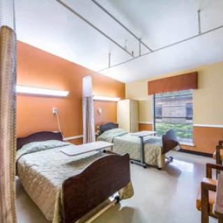 A view of a patient room in a healthcare facility featuring two beds and warm-colored walls.