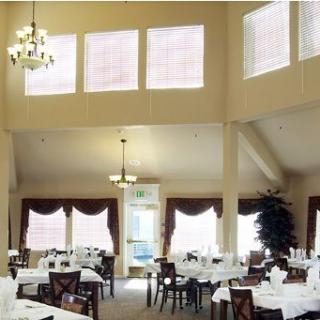 A spacious dining room with elegant chandeliers, neatly arranged tables and chairs, and large windows with curtains.