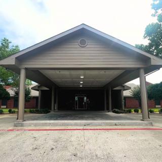 A building entrance with a covered driveway and supporting columns on a clear day.