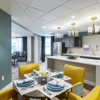 A modern dining room with yellow chairs and an open kitchen, featuring elegant lighting and a stylish table setting.