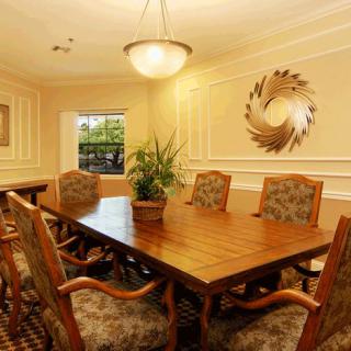 A well-appointed meeting or dining room with a large wooden table, elegant chairs, a decorative wall piece, and a potted plant.