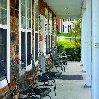 A covered porch with lined chairs against a brick building.