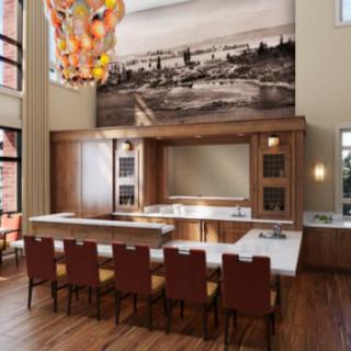 A modern kitchen interior featuring a bar counter with high chairs, wood accents, a vibrant chandelier, and a large artwork adorning the wall.