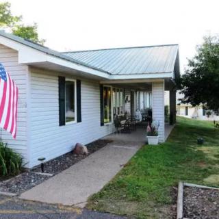 A small house with a porch and an American flag displayed outside, surrounded by a lawn and trees.