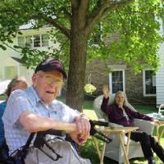 Elderly individuals enjoying a sunny day outdoors in a garden setting.