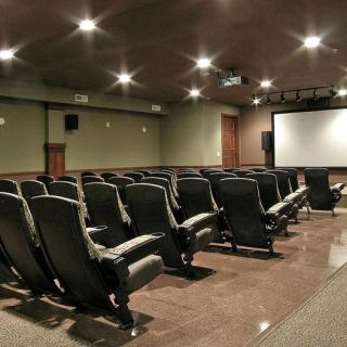 An empty theater room with rows of comfortable seating facing a large screen.