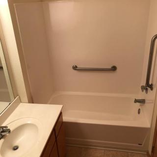 A small bathroom featuring a bathtub with a grab bar, adjacent to a sink and countertop.