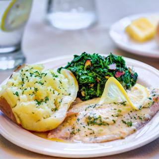 A plated meal featuring fish with lemon slices, sauted spinach, and a baked potato.