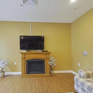 A cozy living room with a wall-mounted television above a wooden fireplace, surrounded by classic decor and a comfortable sofa.