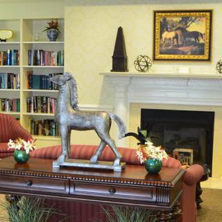 A cozy living room featuring a horse sculpture, surrounding bookshelves, and a fireplace adorned with artwork.