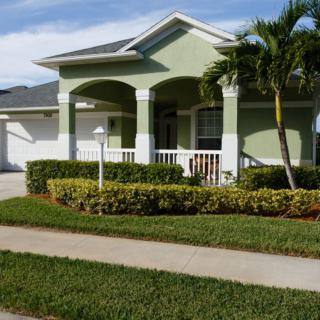 A suburban house with a green exterior, palm tree, and neatly trimmed lawn.