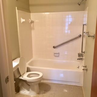 A bathroom featuring a toilet and bathtub with accessibility grab bars installed.
