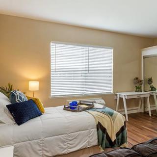 A cozy bedroom with a stylish bed, a desk beside the window, and warm lighting.