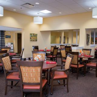 A neatly arranged dining room with multiple tables and chairs, featuring warm lighting and a cozy ambiance.