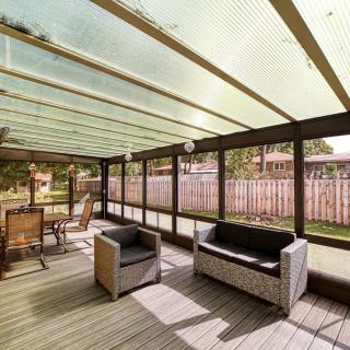 A cozy patio sunroom with glass roofing, featuring comfortable outdoor seating and a view of the backyard fence.