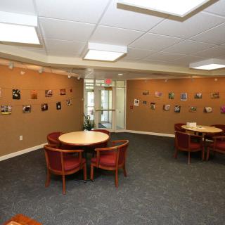 A waiting area featuring round tables with chairs, art displayed on the walls, and a carpeted floor.