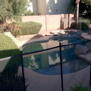 A backyard with a fenced swimming pool and neatly trimmed bushes.