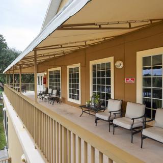 A covered balcony with comfortable chairs and large windows overlooking the exterior.