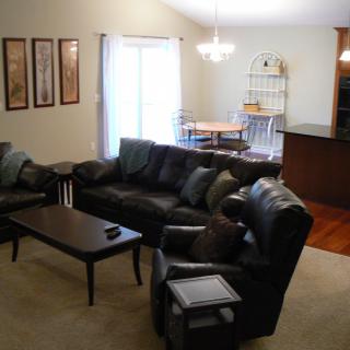 A cozy living room with a black leather sofa set and a coffee table, adjacent to an open dining area.