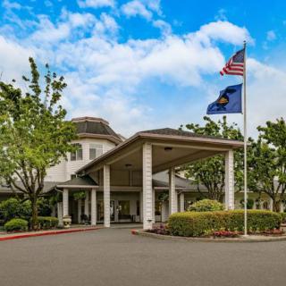 A well-maintained building entrance with flags flying and neatly landscaped surroundings under a cloudy sky.
