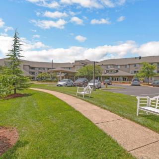 A view of a large building with a neatly maintained lawn, trees, and benches, adjacent to a parking lot.