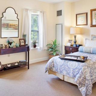 A cozy bedroom with elegant decor, featuring a bed, mirror, nightstand, and framed artwork.