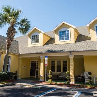 A yellow building with a pitched roof and multiple windows, featuring a palm tree in front and an adjacent parking lot.