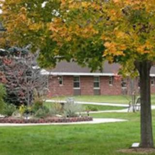 A serene view of a pathway surrounded by trees with autumn foliage and a brick building in the background.