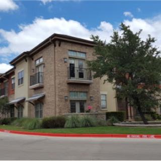 A modern residential building with stylish architecture and well-maintained landscaping under a blue sky.