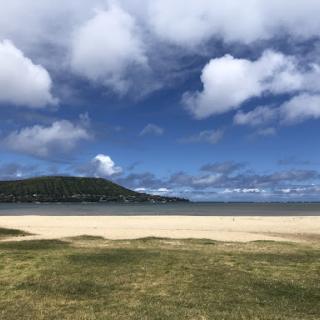 A serene beach view with a blue sky, fluffy clouds, and a stretch of golden sand.