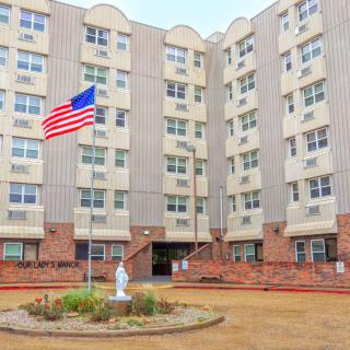 An exterior view of a multi-story apartment building with an American flag and a small statue in front.