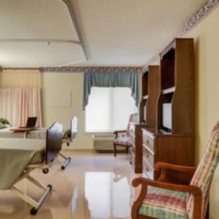 A hospital room with a bed, chairs, and a shelf unit.