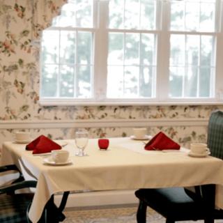 A cozy dining area with a neatly set table, featuring red napkins and natural light streaming through the window.