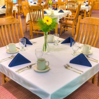 A neatly set restaurant table with blue napkins and a vase of flowers.
