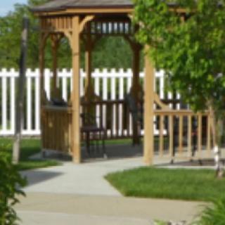 A wooden gazebo in a garden setting with a white fence and trees.