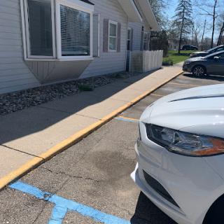 A white car parked in a lot next to a building with a sidewalk.