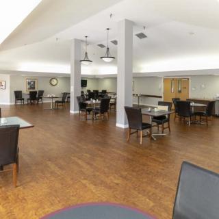 A spacious dining area with tables and chairs arranged neatly on a hardwood floor, illuminated by ceiling lights.