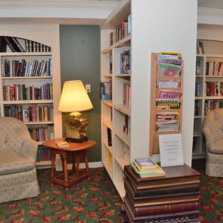 A cozy library reading area with bookshelves, comfortable chairs, and a lamp.
