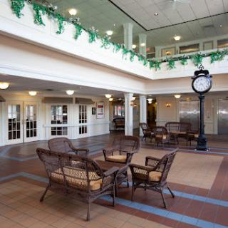 A spacious indoor seating area featuring comfortable wicker furniture and a decorative clock, adorned with greenery.