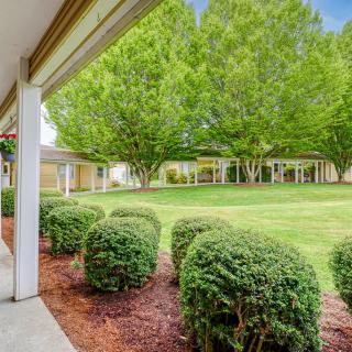 A peaceful garden with neatly trimmed shrubs and lush green trees surrounding a spacious lawn.