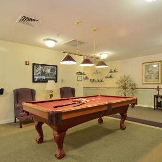 A cozy game room featuring a classic pool table with overhead lighting and comfortable seating.