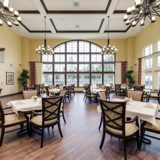 A spacious dining area with elegant chandeliers, neatly arranged tables and chairs, and large windows allowing natural light to flood the room.