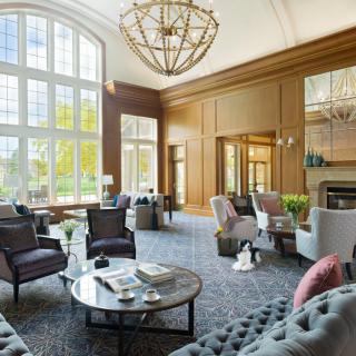 A luxurious and modern living room with large windows, elegant wood paneling, and a central chandelier.