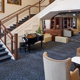A spacious lobby with a grand piano, staircase, and comfortable seating.