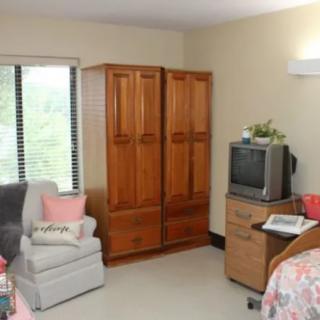 A cozy bedroom with a wooden wardrobe, comfortable chair, and an old-style TV near the window.