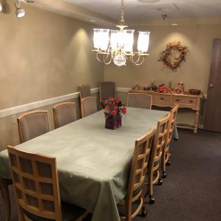 A cozy dining room featuring a long table covered with a tablecloth, surrounded by chairs, and illuminated by a chandelier.
