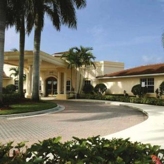 A tropical building surrounded by palm trees and a circular driveway.