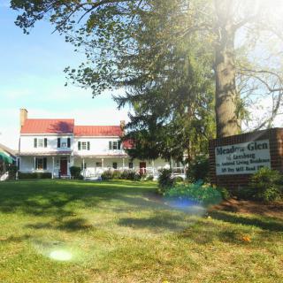 A large building with a red roof, surrounded by trees and a well-kept lawn, featuring a sign in the foreground.