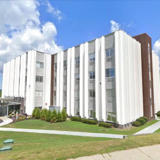 A modern office building with a white facade under a cloudy blue sky.