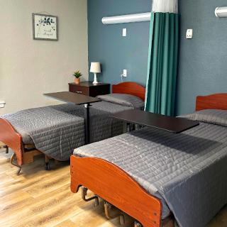 A neatly arranged hospital patient room featuring multiple beds and a calm color scheme.